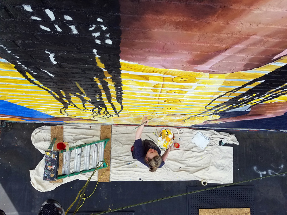 Artist Bonnie Lee Turner painting a mural on the exterior of Beacon Charter High School for the Arts in Woonsocket Rhode Island