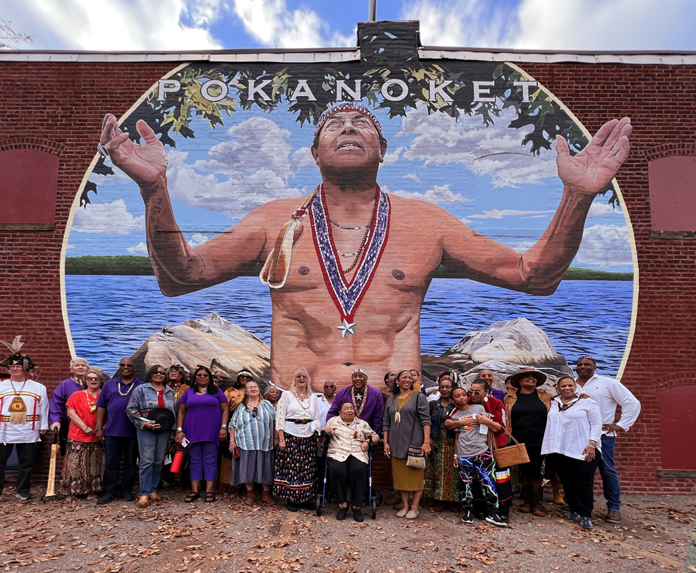 Members of the Pokanoket Tribe standing in front of mural of Metacomet